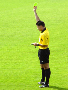 El árbitro amonestando a una jugadora con la tarjeta amarilla
