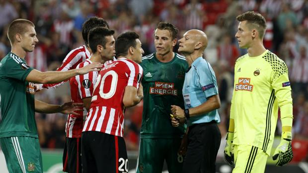 Los jugadores del Athletic rodean al árbitro del partido ante el Rapid